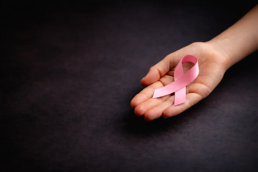 Hand mit rosafarbener Schleife zum Weltkrebstag vor dunklem Hintergrund