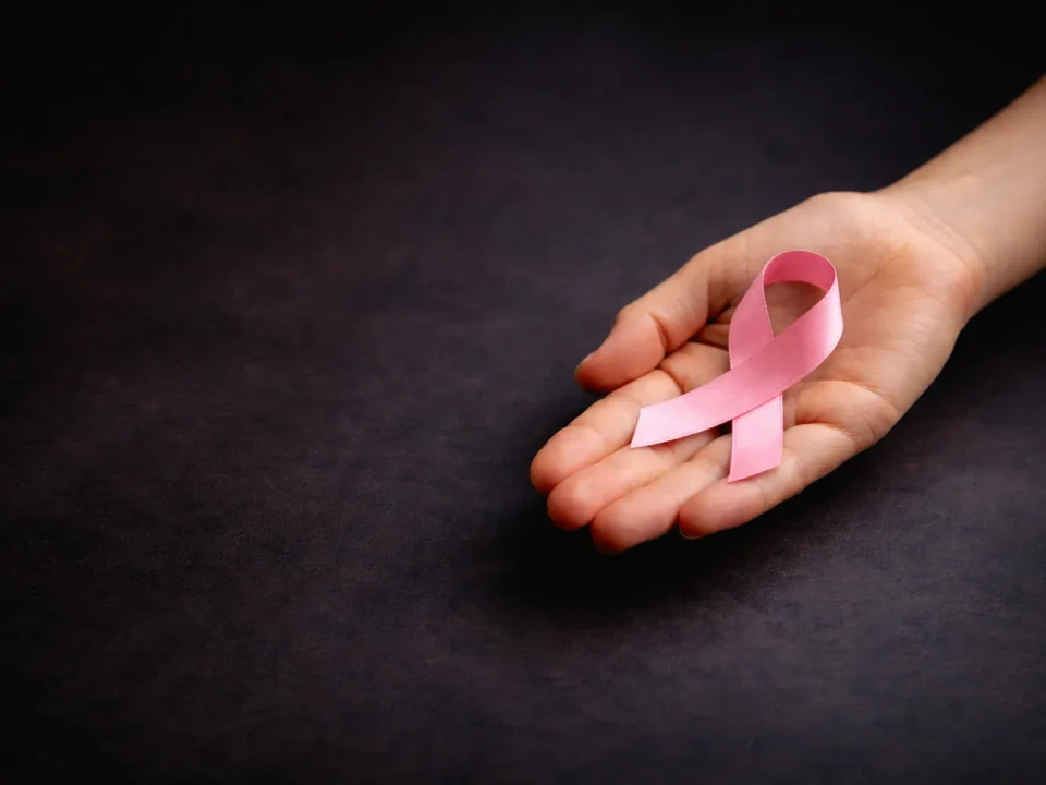 Hand mit rosafarbener Schleife zum Weltkrebstag vor dunklem Hintergrund