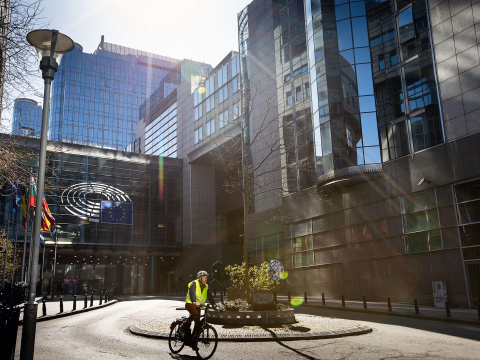Parlamentsgebäude in Brüssel im Sonnenschein, vorne ein Kreisverkehr mit Fahrradfahrer